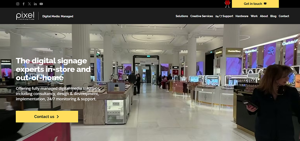Showroom-style retail space with multiple digital signage displays along the aisles; overlay headline reads 'The digital signage experts in-store and out-of-home' with a yellow 'Contact us' button beneath.