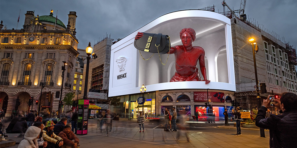 Nighttime city square with a large digital billboard displaying a red statue and a Versace handbag.