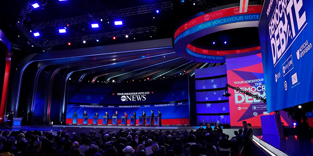 Novastar VX1000 Pro-Concert tours Large televised debate stage with multiple panelists seated at a long table, audience watching in a darkened auditorium.