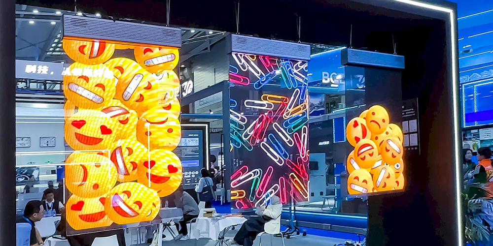 Trade show booth with large emoji panels and a neon light wall; people sit at white tables inside.