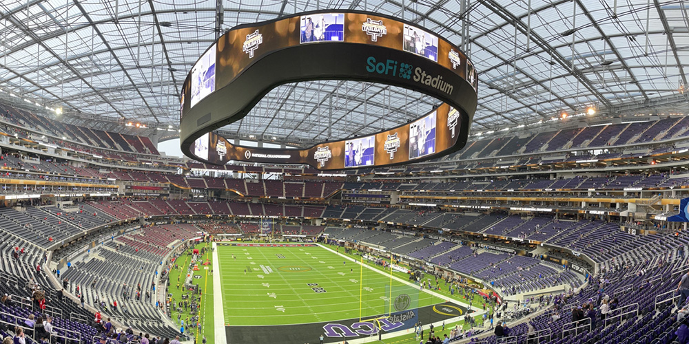 体8 Interior of SoFi Stadium with a large circular video board overhead and rows of purple seats surrounding a green football field, empty during setup.