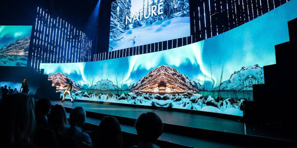 接 - LED Screen Board - LED Screen Board Stage with curved LED backdrop showing snowy mountains and the word NATURE; audience seated in front.