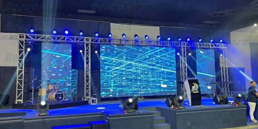 水 - LED Screen Board - LED Screen Board Stage with three large LED screens, blue lights, and a drum kit on the left at an indoor event beyond the audience.
