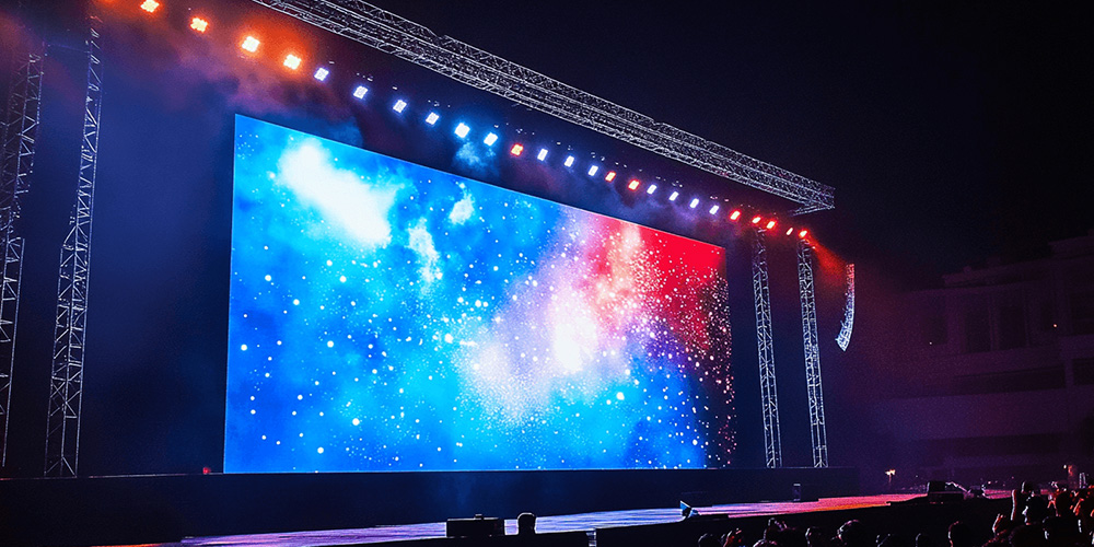 租4y - LED Screen Board - LED Screen Board Outdoor concert stage at night with a giant LED screen showing a blue cosmic image and colorful stage lights, truss rig above.
