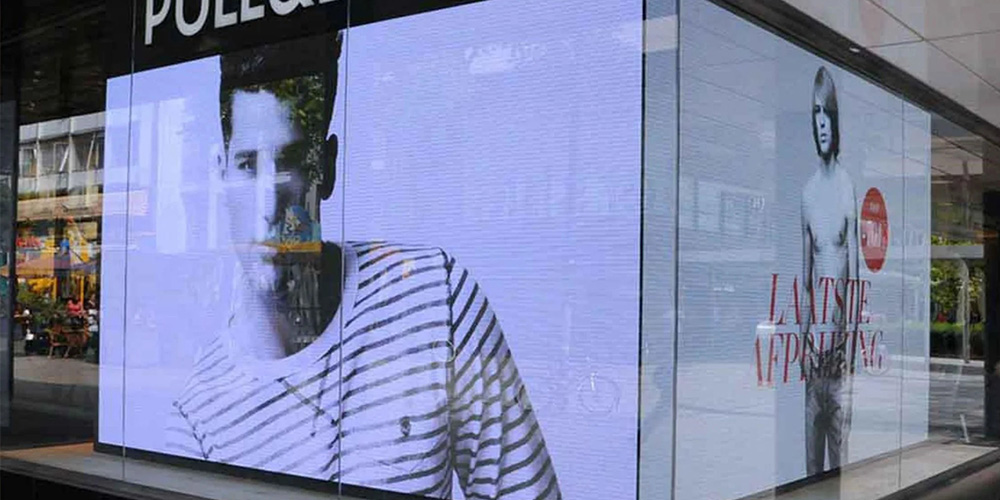 Storefront window with a large digital display showing a man in a striped shirt; another poster shows a shirtless model with red text.