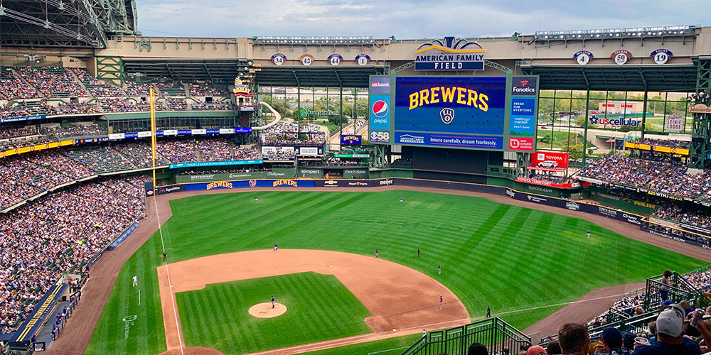 Wide view of a Milwaukee Brewers baseball game at American Family Field, packed stands, scoreboard displaying 'BREWERS' above the field.