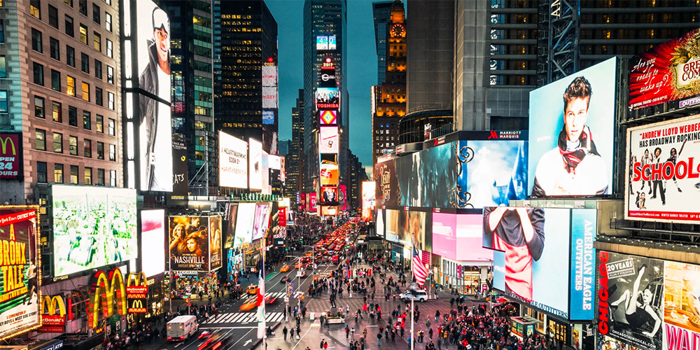 Busy nighttime view of Times Square with neon billboards and crowds on the streets in a bustling city square.