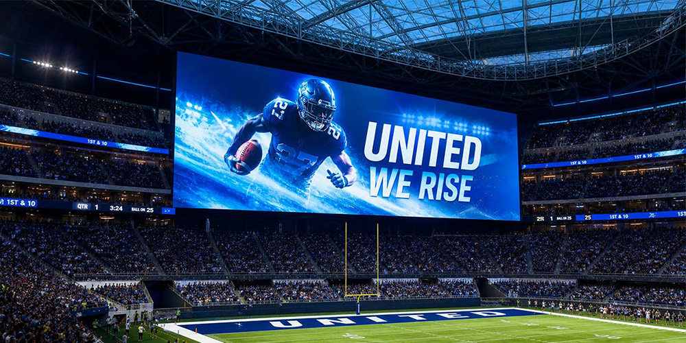 Football stadium with a giant blue screen showing a football player and the words 'UNITED WE RISE'.