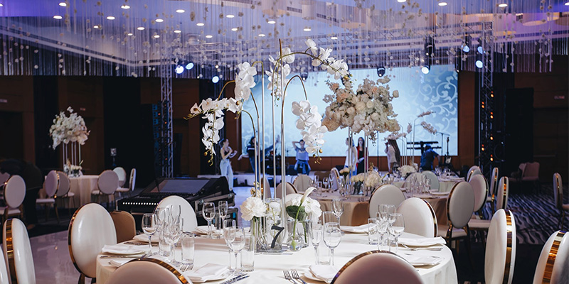 室内婚礼屏幕1 - LED Screen Board - LED Screen Board Elegant banquet hall with round tables, white floral centerpieces, and a stage with performers in the background.