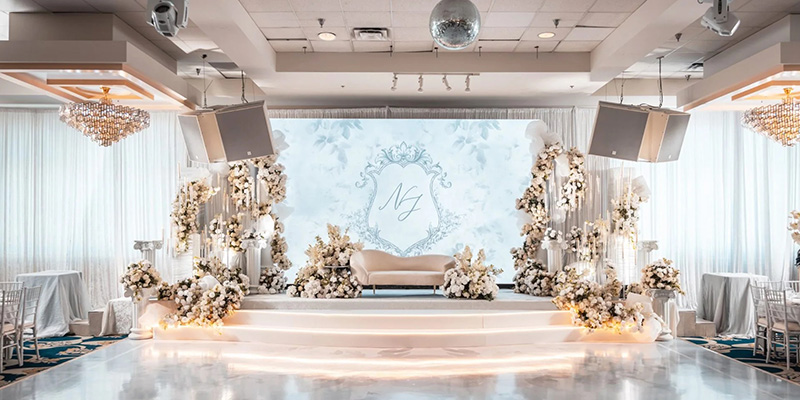 室内婚礼屏幕4 - LED Screen Board - LED Screen Board Elegant wedding reception stage with white cream floral arrangements, a cream sofa, and a light blue monogram backdrop.