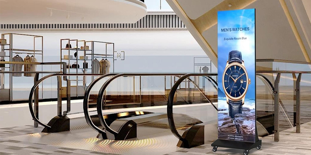 海报屏1 - LED Screen Board - LED Screen Board Tall digital ad display featuring a blue-faced men's watch on a rocky ocean backdrop beside an escalator in a sleek mall.