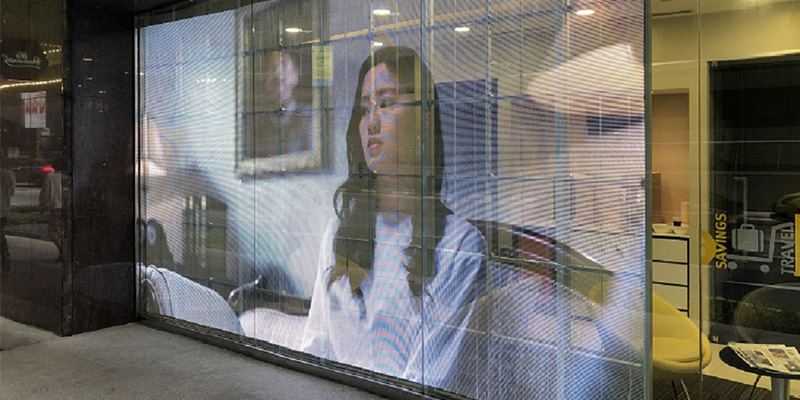 透明屏幕2 - LED Screen Board - LED Screen Board Digital billboard on a storefront window shows a woman in a white blouse; reflections and interior visible through glass panels.