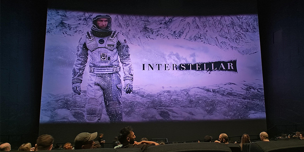 01-IMAX-Melbourne - LED Screen Board - LED Screen Board Movie theater screen showing a large Interstellar poster with an astronaut on a snowy alien world, audience seated in the dark foreground.