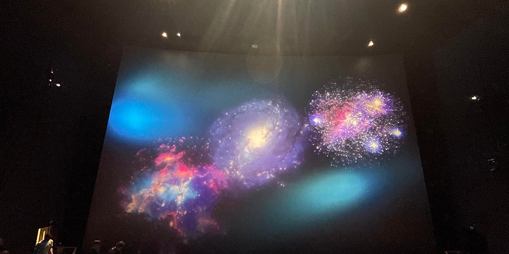 05-Airbus-IMAX-Theater - LED Screen Board - LED Screen Board Curved screen in a dark room showing three colorful galaxy-like projections with blue, purple, and pink nebulae and starbursts.
