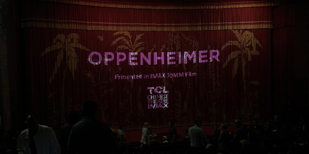 07-TCL-Chinese-Theatre-IMAX - LED Screen Board - LED Screen Board Stage with a red-curtain backdrop and a pink projection reading 'OPPENHEIMER'—'Presented in IMAX 70MM Film' with audience silhouettes in the foreground.