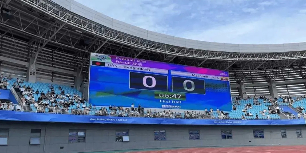 Large outdoor stadium with blue seating and a giant electronics scoreboard showing a 0–0 football match between Bangladesh (BAN) and Myanmar (MYA) in the first half, time 06:47.