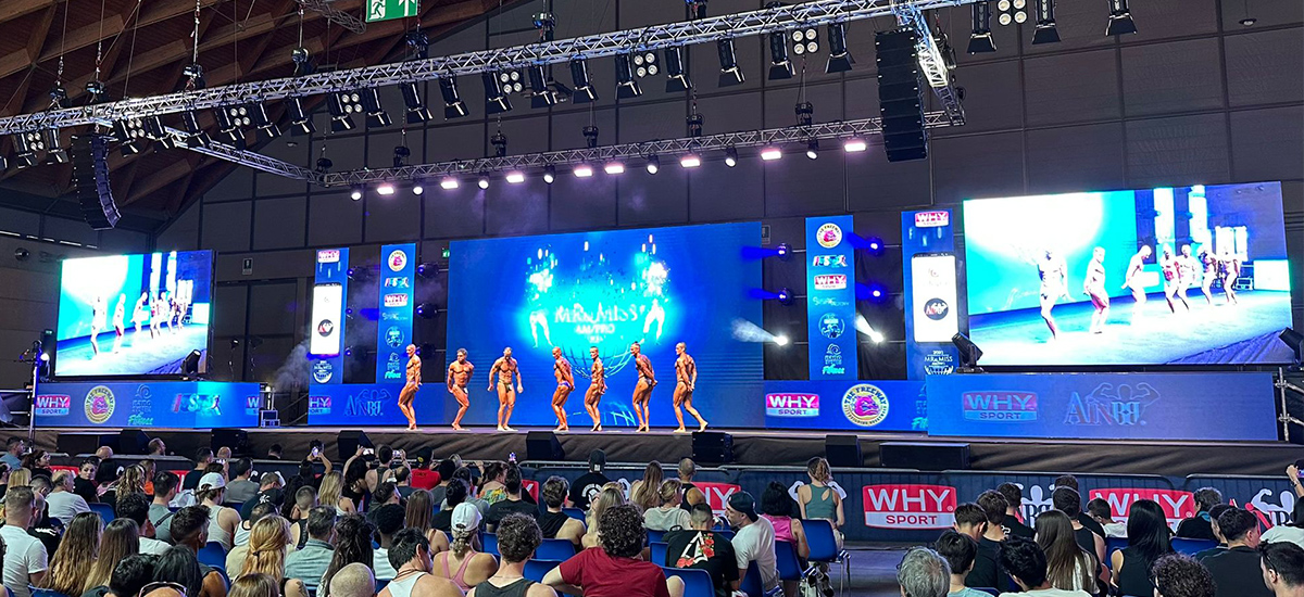 Event-LED-Screen-6 - LED Screen Board Bodybuilders posing on a large stage with bright screens and an audience watching a competition.