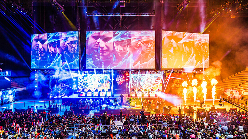 Event-LED-Screen-8 - LED Screen Board Esports stadium scene with three large screens, players on stage, and a crowded audience.