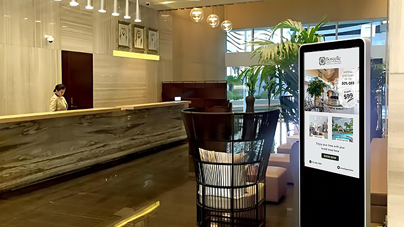 Lobby - LED Screen Board Hotel lobby with a marble reception desk, seated staff, and a tall digital directory screen on the right showing promos.