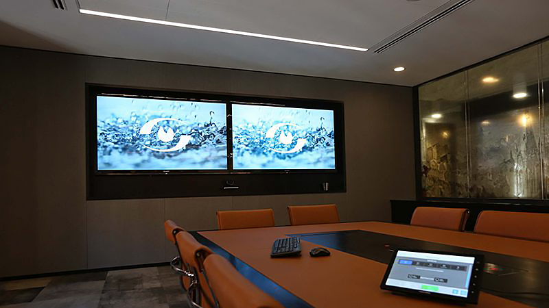 Meeting-Rooms - LED Screen Board Modern conference room with orange chairs around a long table; two wall screens display a blue water splash logo.