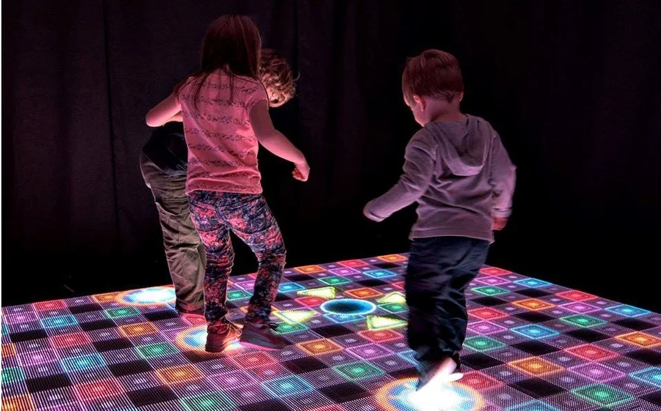 Children standing on an LED floor showing colorful geometric patterns